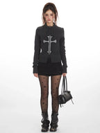 Woman wearing a dark grey knit zip-up cardigan with a large grey embroidered cross on the front.