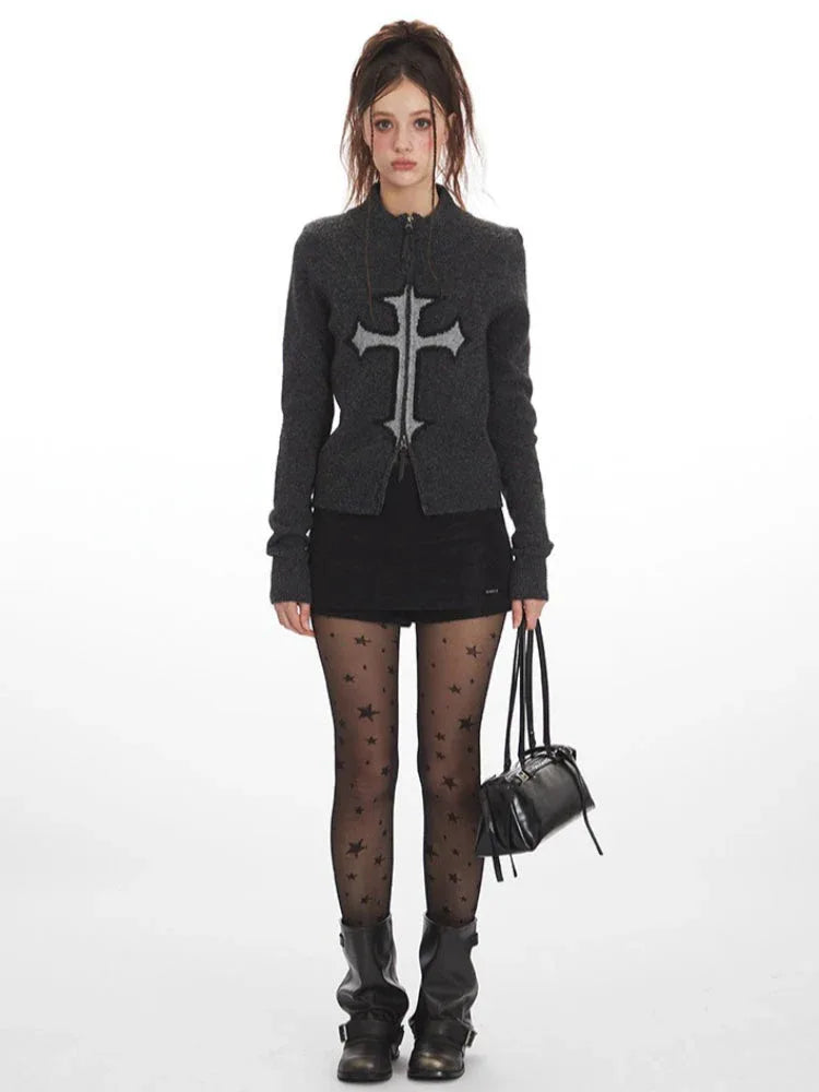 Woman wearing a dark grey knit zip-up cardigan with a large grey embroidered cross on the front.