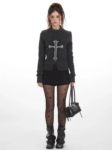 Woman wearing a dark grey knit zip-up cardigan with a large grey embroidered cross on the front.
