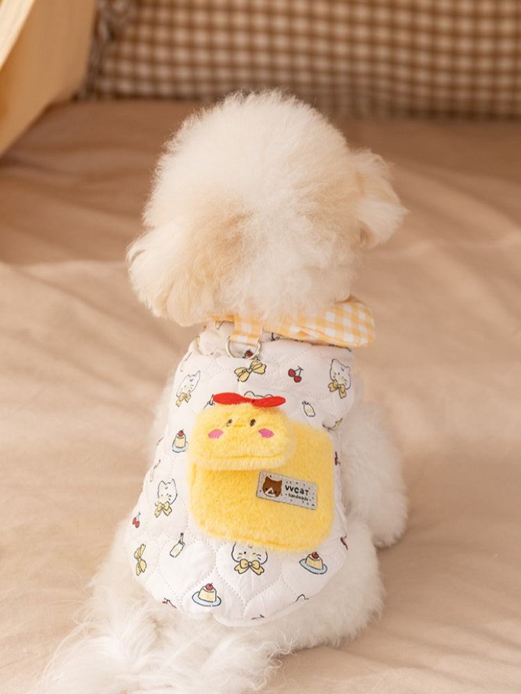 Back view of a white bichon frise dog wearing a white quilted vest with a yellow pocket and cartoon prints