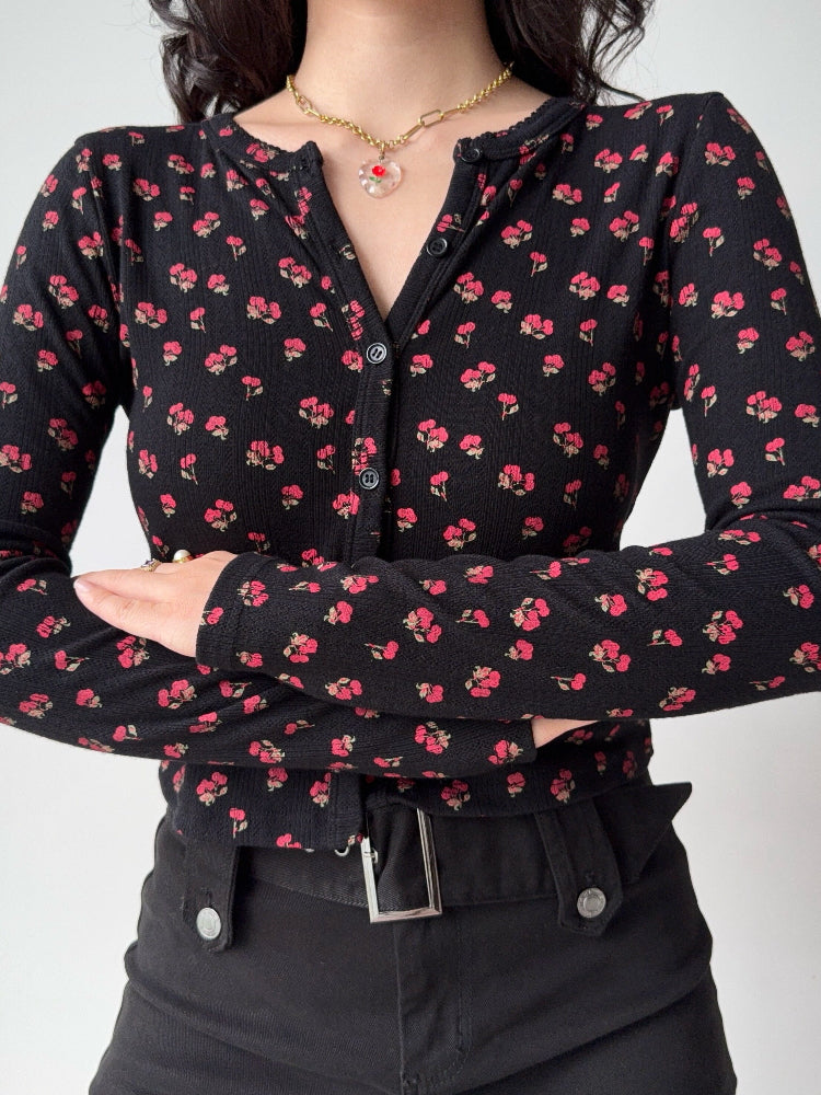 Close-up of a woman wearing a black long-sleeve cardigan with a small pink floral print.