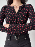 Woman with arms crossed wearing a black button-up cardigan with a floral pattern.