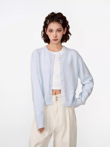 Woman wearing a light blue cropped knit cardigan with a crew neckline and button-front closure.