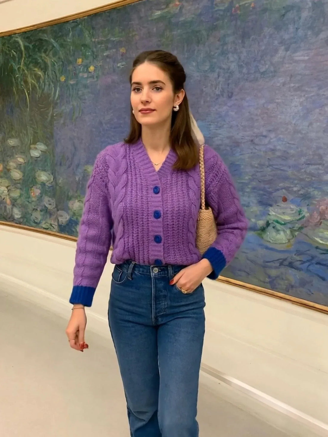 Woman wearing a purple cable knit cardigan with blue buttons and cuffs, paired with blue denim jeans.