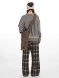 Back view of a woman wearing a grey knit sweater with a graphic sheep print and plaid wide leg pants.