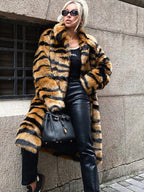 Woman wearing a long faux fur coat with tiger stripes and black pants.