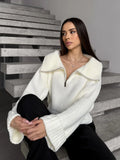 Woman sitting on stairs wearing a white knit cropped sweater with a half-zip closure.