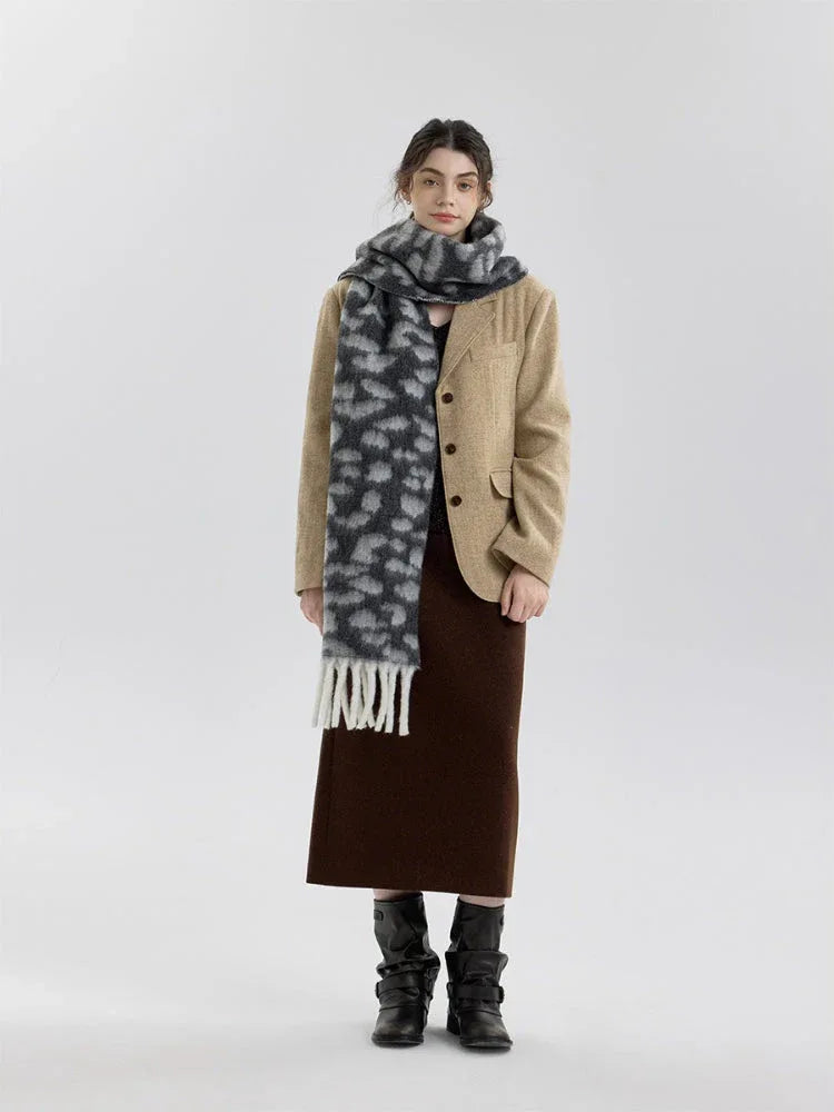 Woman wearing a beige blazer, brown skirt, and a grey and white leopard print fuzzy scarf with fringe trim.