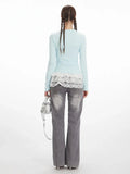 Back view of a woman in a light blue long-sleeve top with white lace trim and grey wide-leg jeans