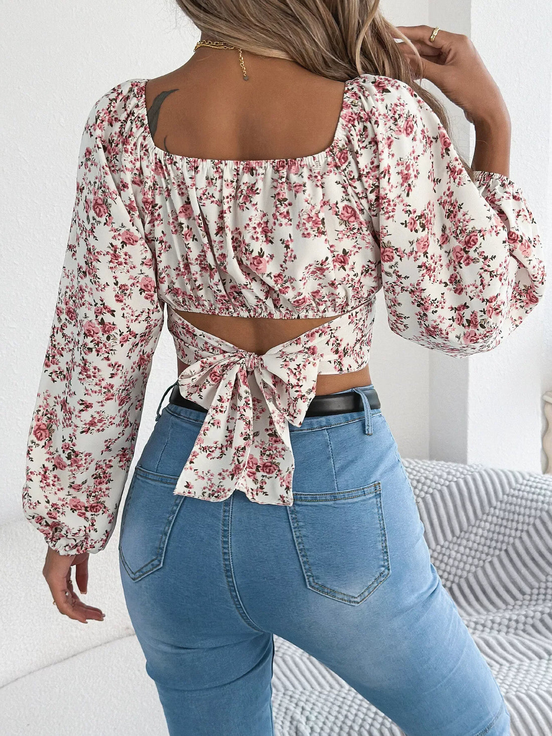 Woman wearing a white floral print cropped top with long puff sleeves and a square neckline.