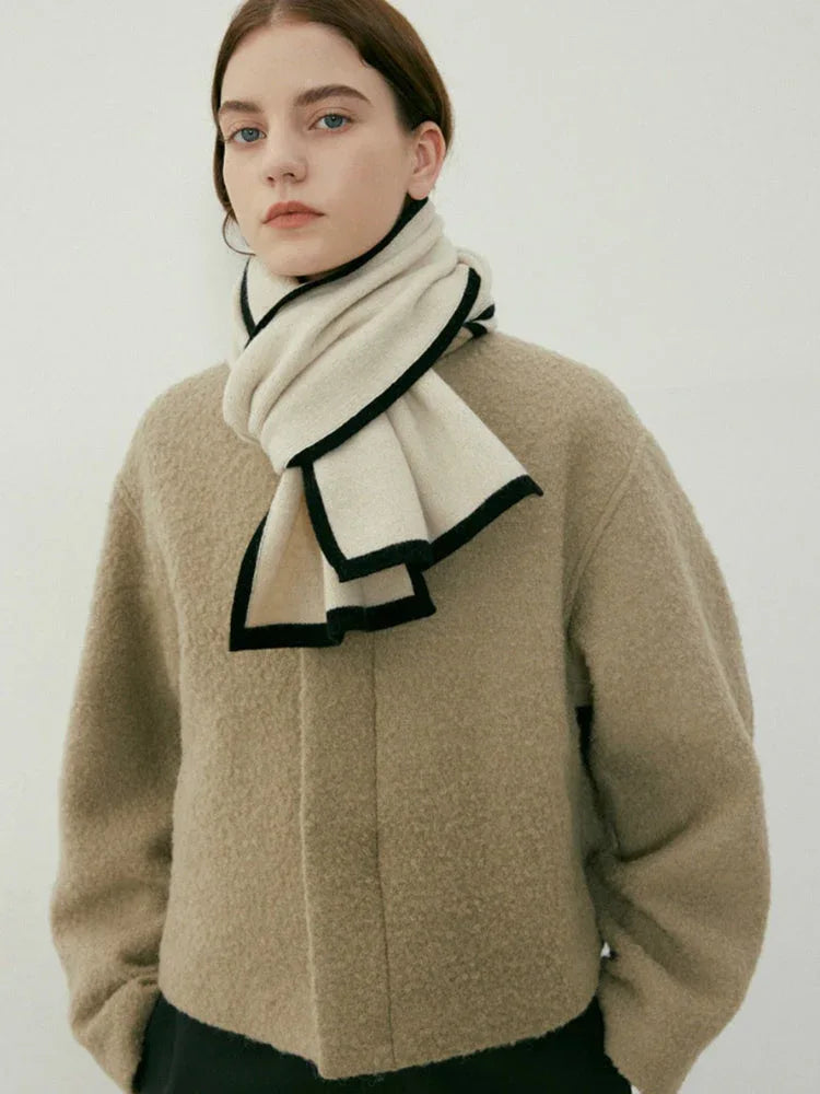 Model wearing a cream knit scarf with black trim around the neck