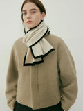 Model wearing a cream knit scarf with black trim around the neck