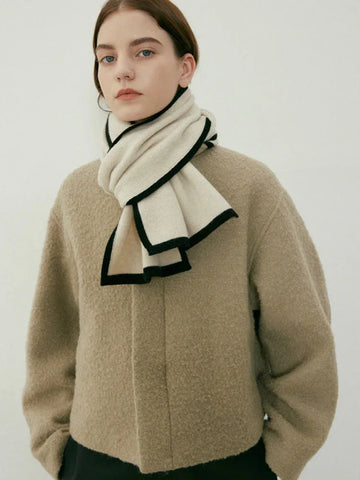 Model wearing a cream knit scarf with black trim around the neck