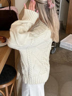 Woman wearing a cream cable knit sweater and white pants, showing the textured knit detail.