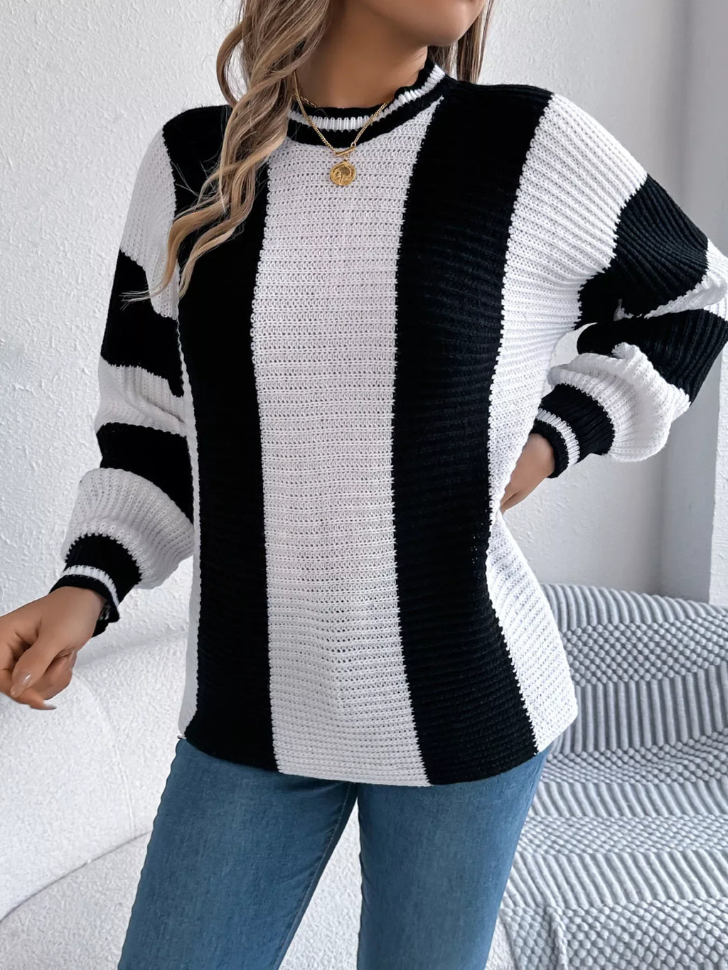 Close-up of a woman wearing a black and white striped knit sweater and blue jeans, with one hand on her hip.