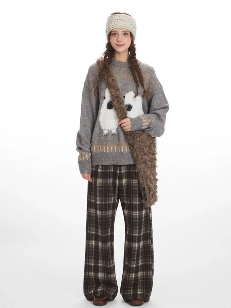 Woman wearing a grey knit sweater with a graphic sheep print and plaid wide leg pants, holding a faux fur bag. Main image