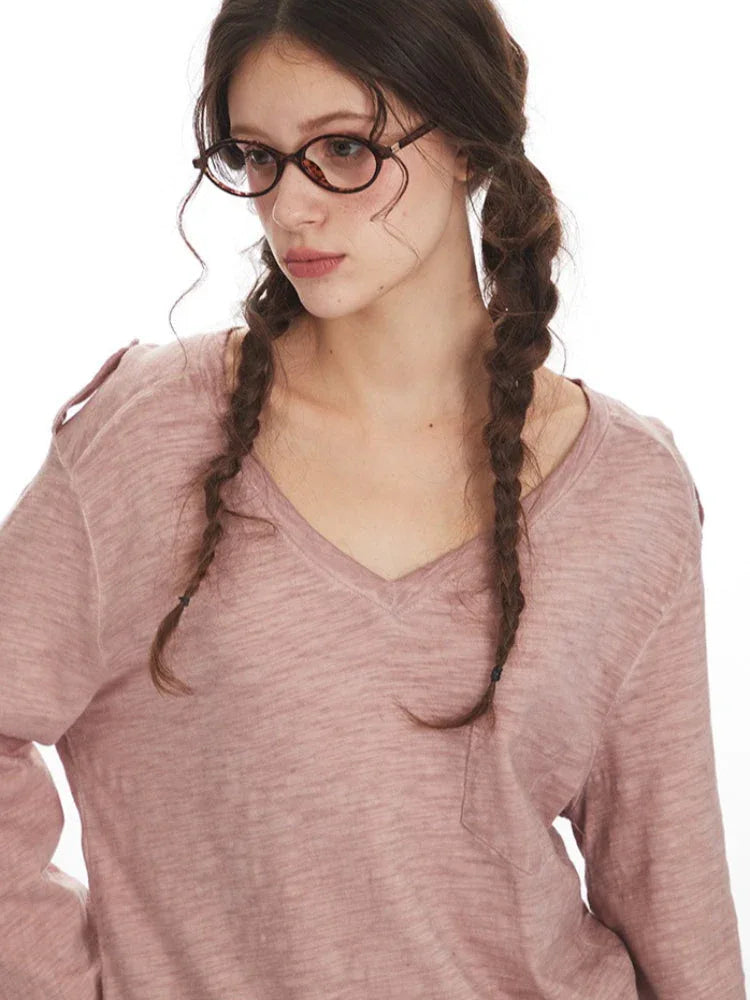 Close-up of a woman's face and shoulders wearing a dusty rose long-sleeve knit top with a V-neck. She has braids and glasses.