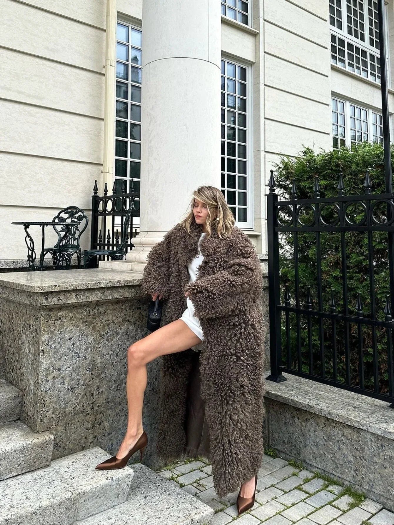 Model posing in a long brown faux fur coat outdoors.