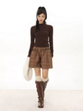 Woman wearing a brown long-sleeve mock neck top with plaid shorts and brown boots.