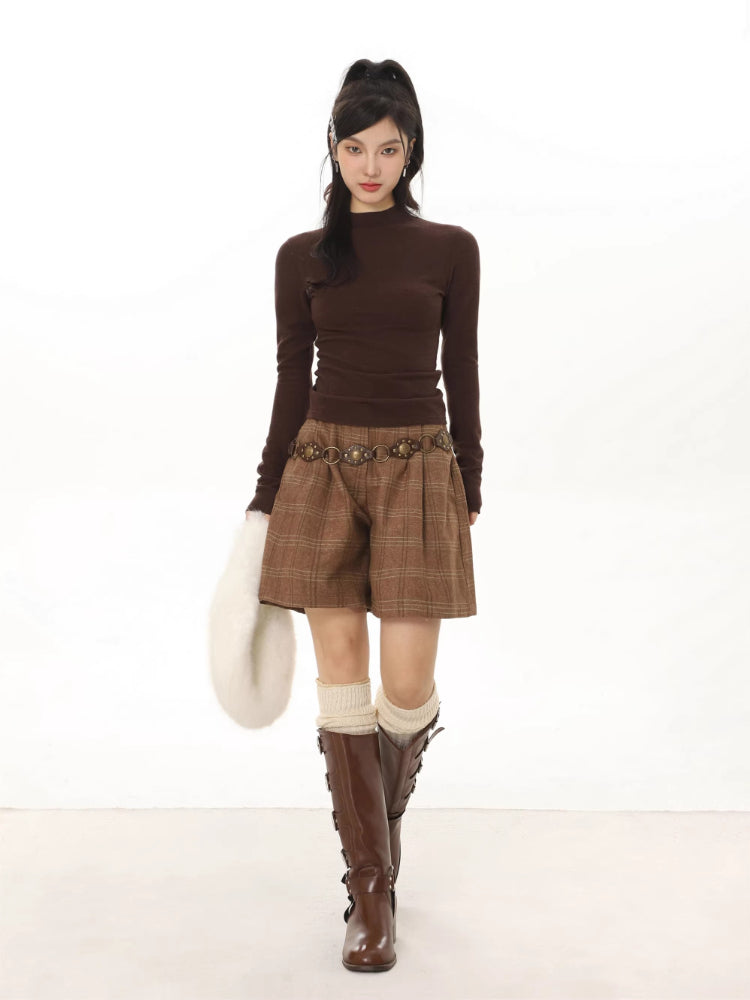 Woman wearing a brown long-sleeve mock neck top with plaid shorts and brown boots.