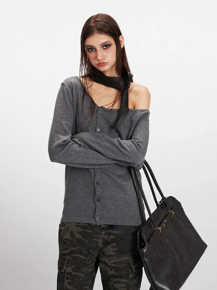 Close-up of a woman wearing a grey knit cardigan with an asymmetrical neckline and a black scarf.