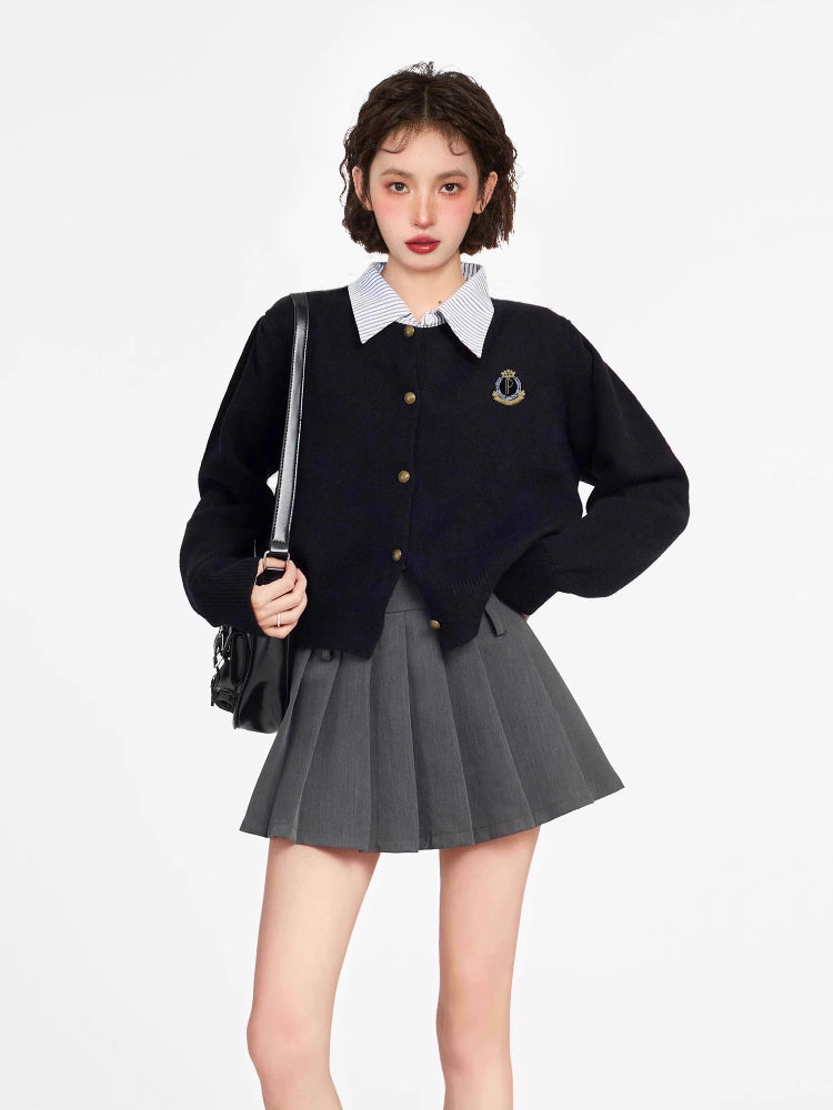 Woman wearing a black knit cardigan with a collared neckline and button-up front, paired with a grey pleated skirt.