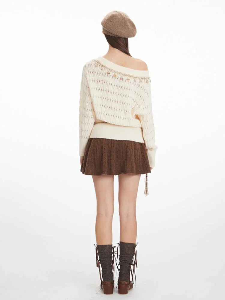 Back view of a model wearing a cream-colored off-the-shoulder knit sweater with a diamond pattern and decorative trim. The sweater is paired with a brown textured mini skirt and brown knee-high socks.