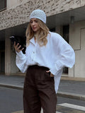 Woman in white oversized cotton shirt looking at her phone