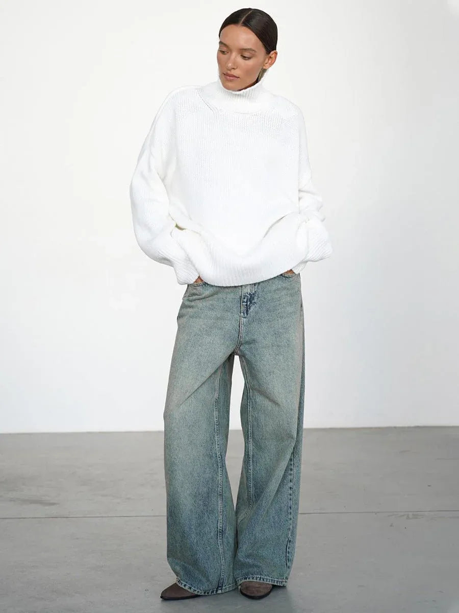 Woman wearing a white oversized high neck ribbed knit sweater with wide-leg jeans