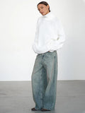 Model with hands in pockets wearing an oversized white turtleneck sweater