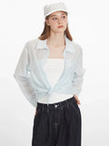 Woman tying the front of a light blue oversized button-down shirt