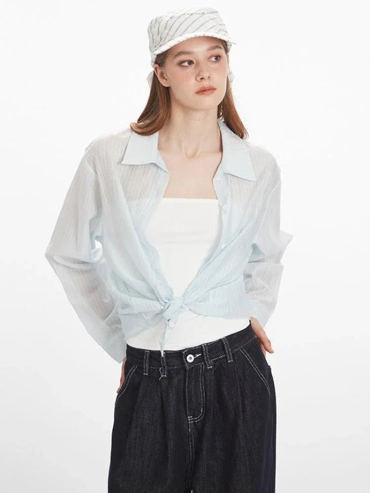 Woman tying the front of a light blue oversized button-down shirt