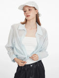 Woman wearing a light blue oversized button-down shirt tied at the waist over a white top