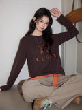 Model posing in a dark brown long sleeve embroidered top and beige pants.