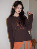 Close-up of a dark brown long sleeve top with contrasting orange letter embroidery.