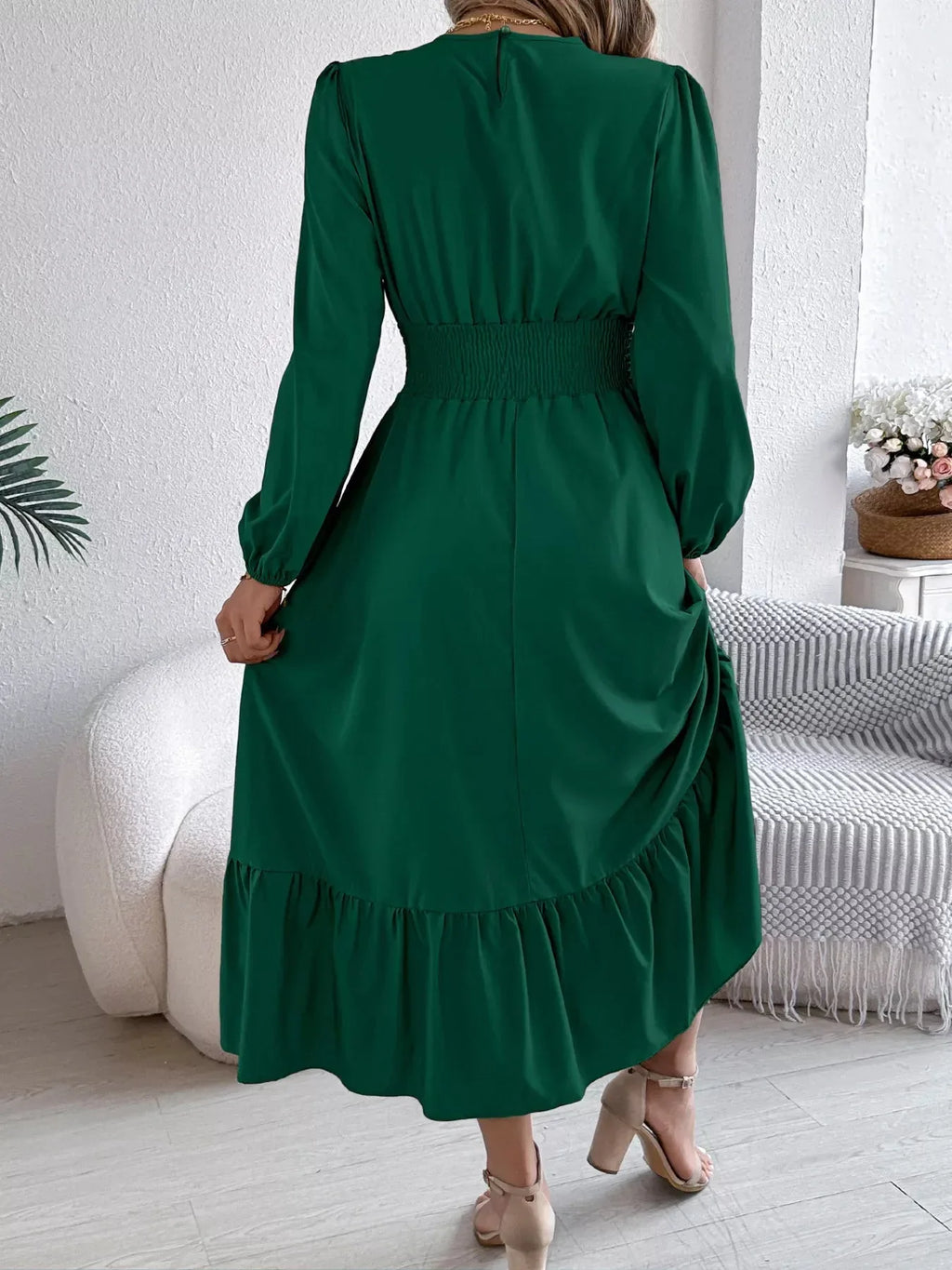 Back view of a woman in a long-sleeved green A-line dress with a tiered, ruffled hem.