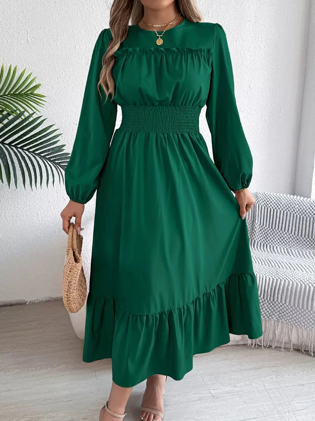 Full view of a woman in a green A-line dress with puff sleeves and a ruffled hem, holding a straw bag.