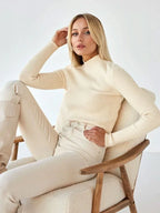 Model posing in a white mock neck sweater and wide-leg denim