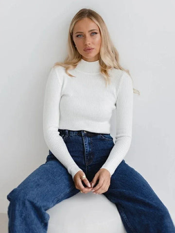 Woman wearing a white ribbed mock neck sweater with blue jeans