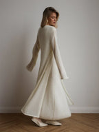 Rear view of a woman in a flowing white knit maxi dress and cardigan