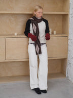 Model wearing a cream and black raglan sleeve sweater with an argyle scarf and white pants.