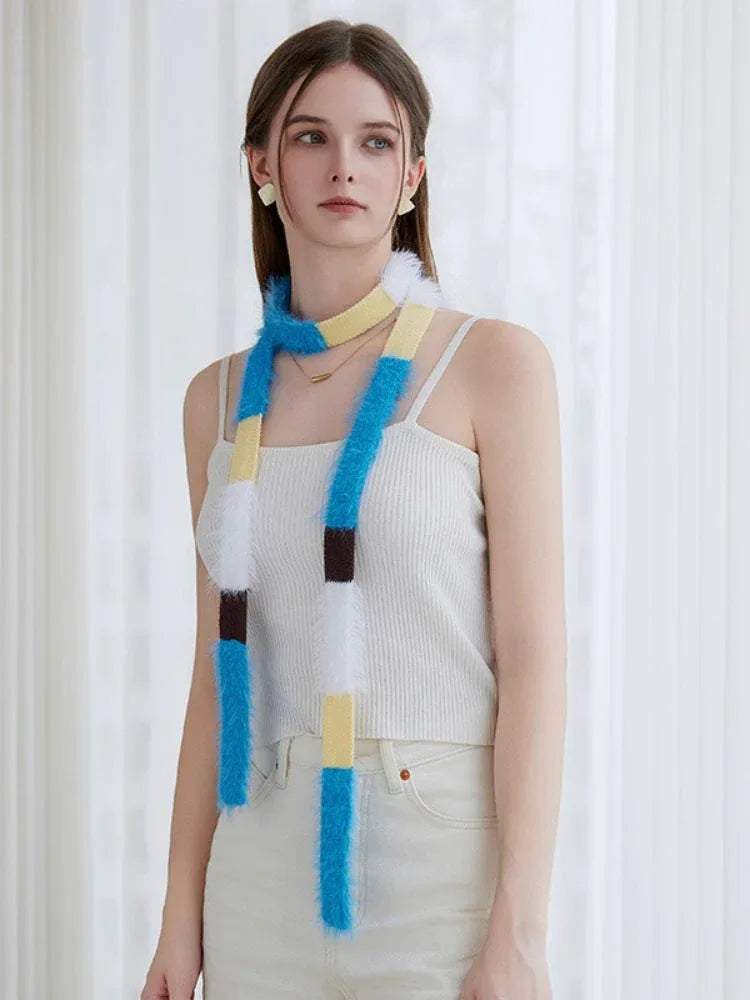 Front view of a woman in a white ribbed camisole and cream pants, showcasing a long, fuzzy knit scarf with horizontal color blocks.