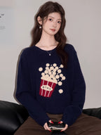 Woman wearing a navy blue knit sweater with a popcorn graphic and Korean text