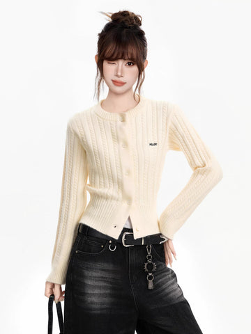 Woman wearing a cream cable knit cropped cardigan with a crew neck and button front, paired with dark wash wide-leg jeans and a black belt.