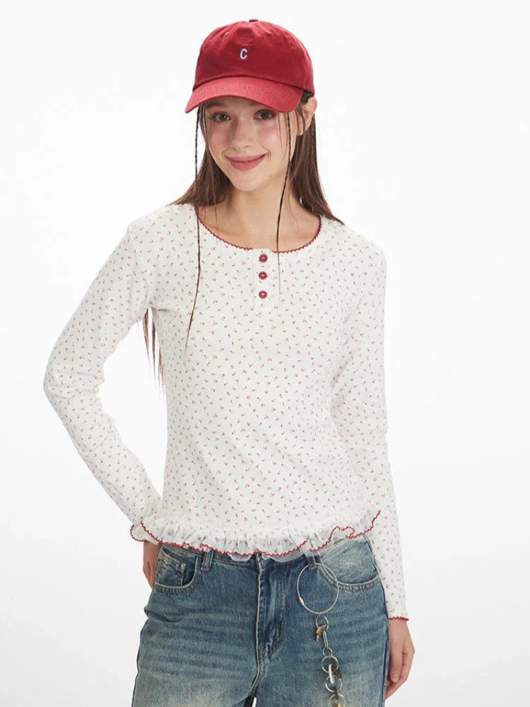 Close-up of a woman wearing a white long-sleeve top with a red floral print, red trim, and three red buttons at the neckline.