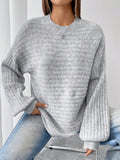 Close-up front view of a woman's torso wearing a light grey oversized knit sweater with textured horizontal stripes.