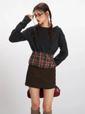 Close-up of a model adjusting glasses, wearing a dark grey knit cropped sweater with a plaid waistband accent.