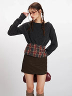 Close-up of a model adjusting glasses, wearing a dark grey knit cropped sweater with a plaid waistband accent.