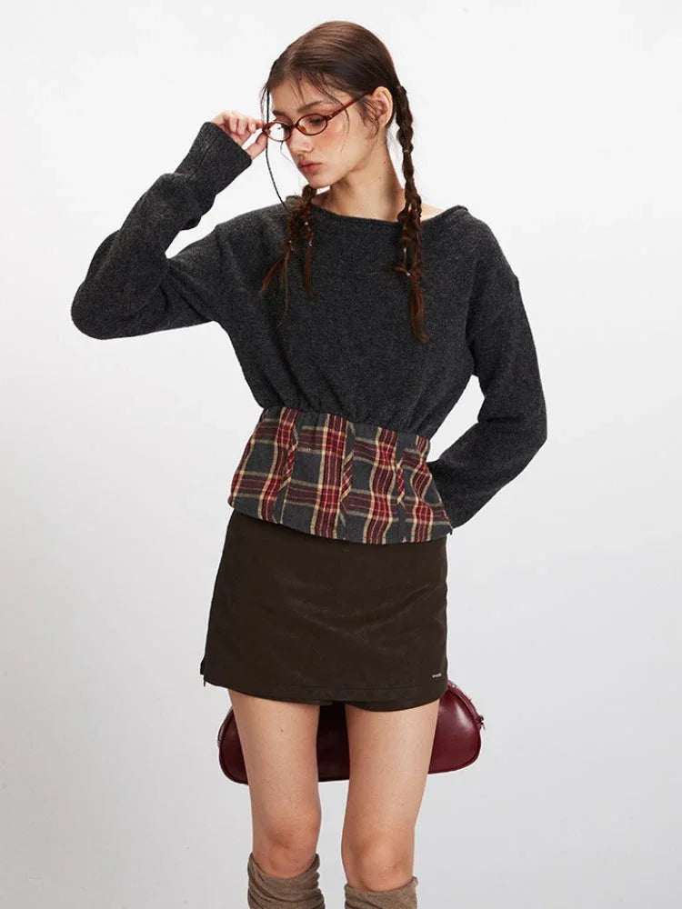 Close-up of a model adjusting glasses, wearing a dark grey knit cropped sweater with a plaid waistband accent.