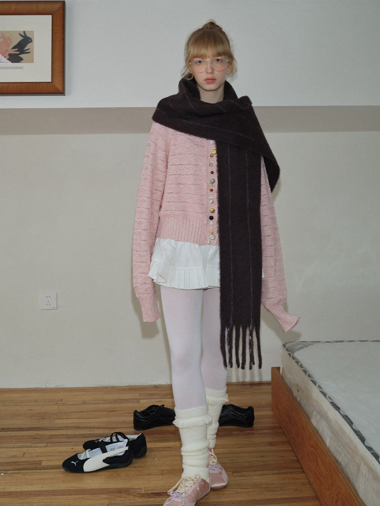 Woman wearing a pink knitted cardigan and a long dark brown scarf, looking towards the camera.